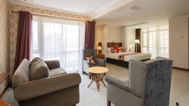 Hotelkamer met een bank, fauteuil, klein rond tafeltje en een bed met kussens en een deken.