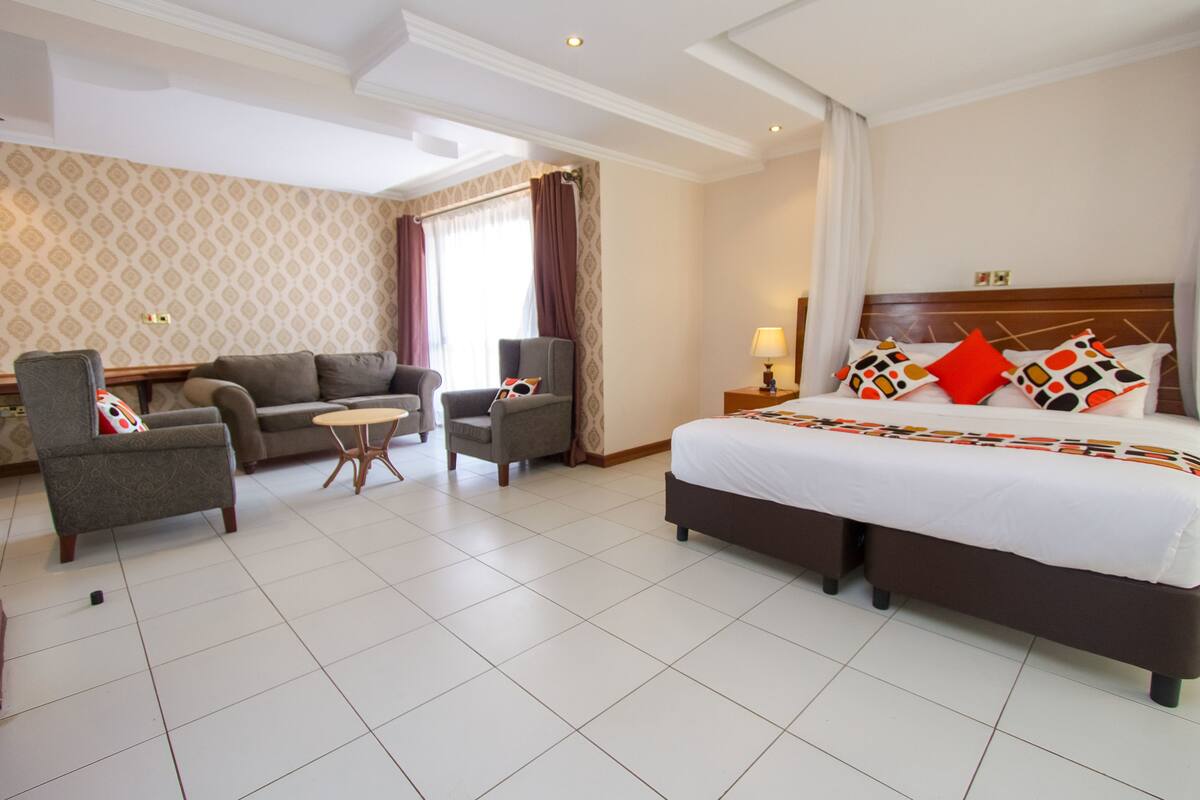 Una habitación de hotel con una cama grande, dos sillones, una mesita redonda y un sofá.