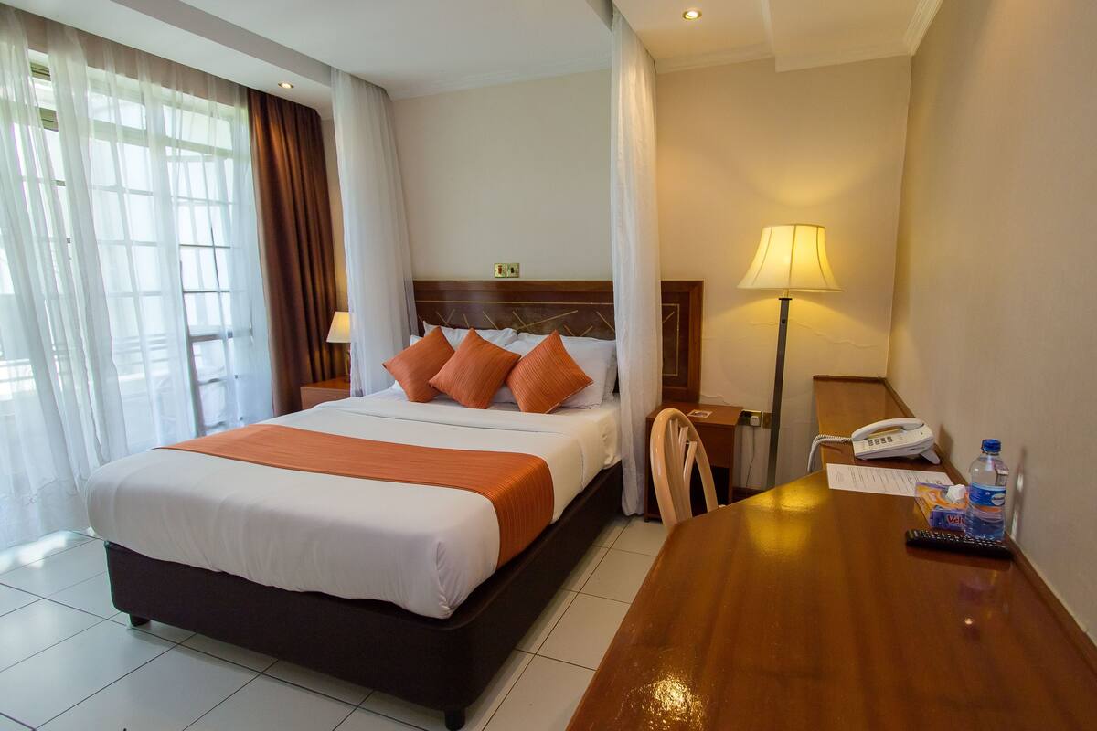 Habitación de hotel con cama, escritorio, lámpara, teléfono y botella de agua.