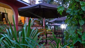 An outdoor seating area with tables and umbrellas, surrounded by lush greenery. - Wigot Gardens (Kisumu)