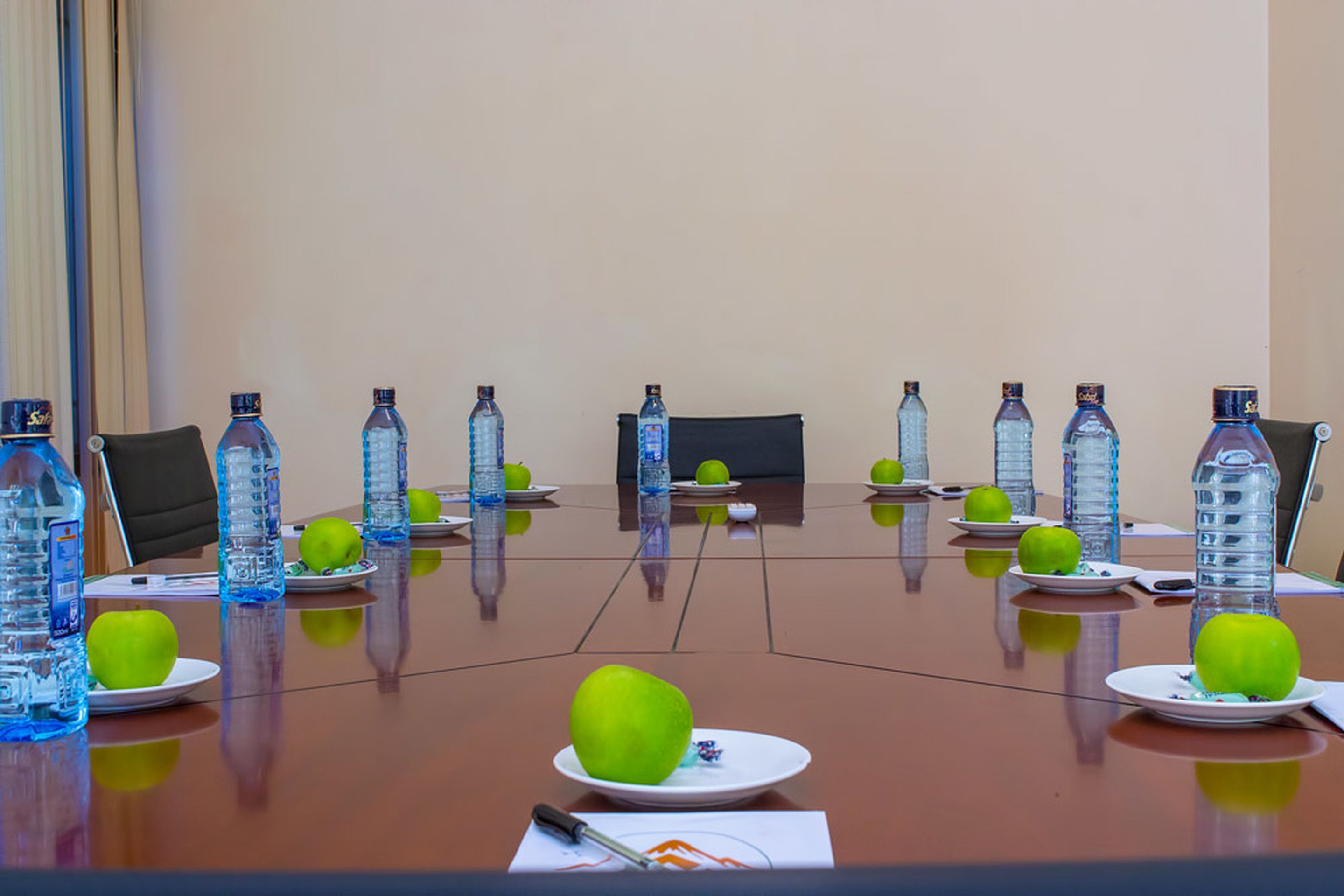 Ett konferensbord med vattenflaskor och äpplen, en bärbar dator och en penna.