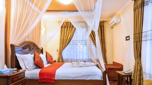 A neatly arranged bedroom with a wooden bed, a bedside table, a chair, and a small table with a phone. - Wigot Gardens (Kisumu)
