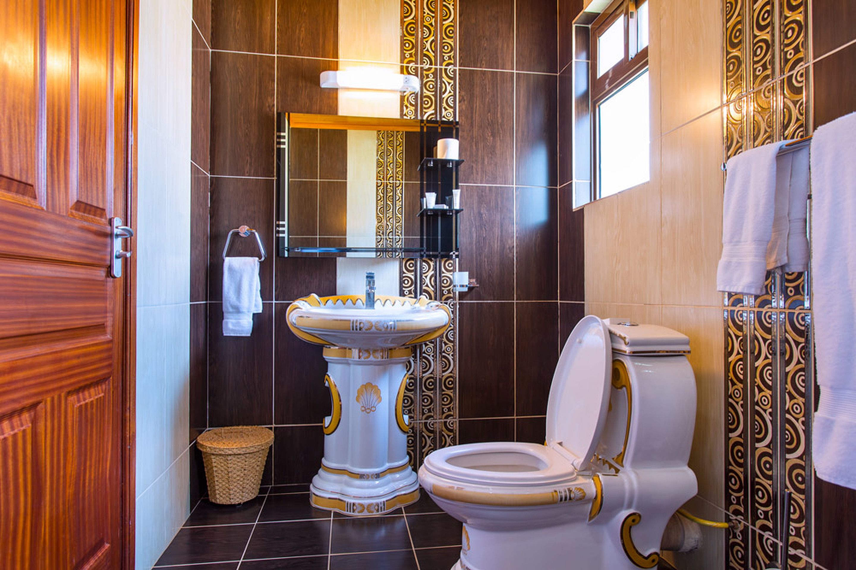A bathroom with a wooden door, a pedestal sink, a toilet, and a mirror.