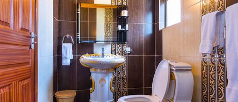 A bathroom with a wooden door, a pedestal sink, a toilet, and a mirror.