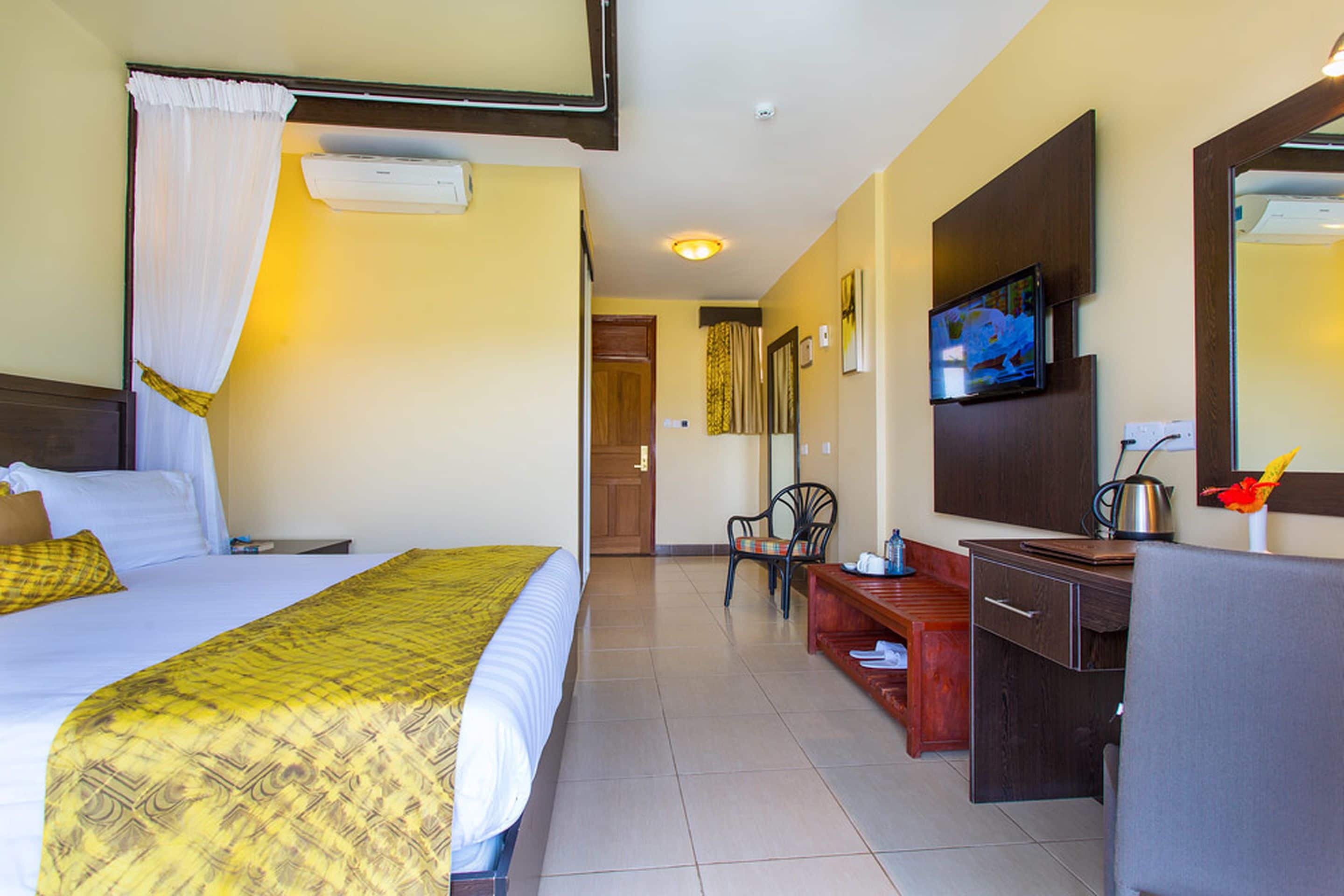 Une chambre d’hôtel avec un lit, un bureau, une chaise, une télévision et une salle de bain visible au fond.