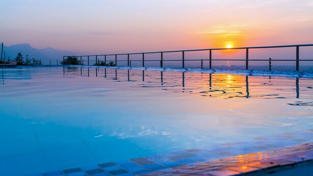 A sunset over a calm body of water with a metal railing in the foreground. - Wigot Gardens (Kisumu)