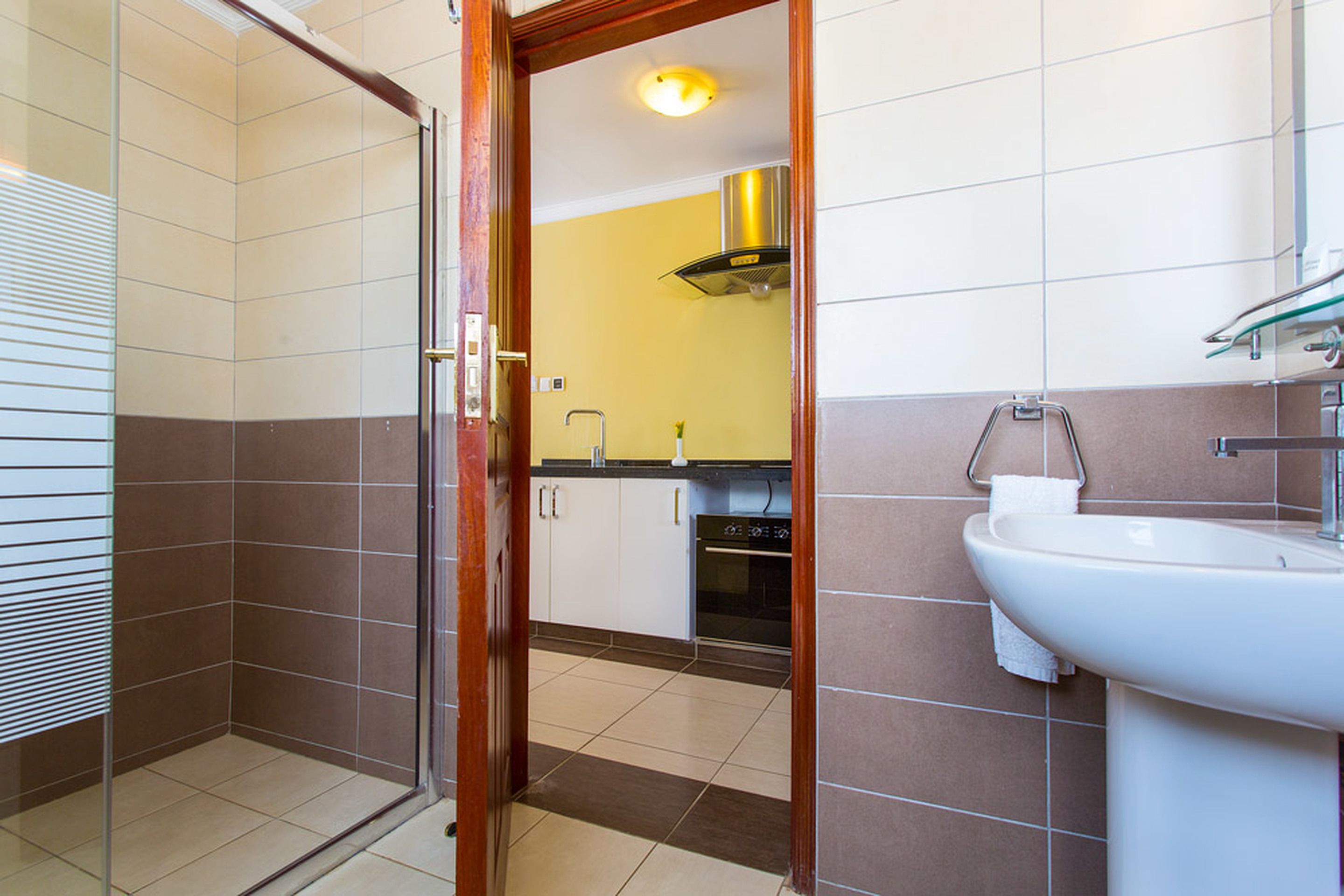 A bathroom with a shower, toilet, sink, and a small kitchen area with cabinets and a stove.