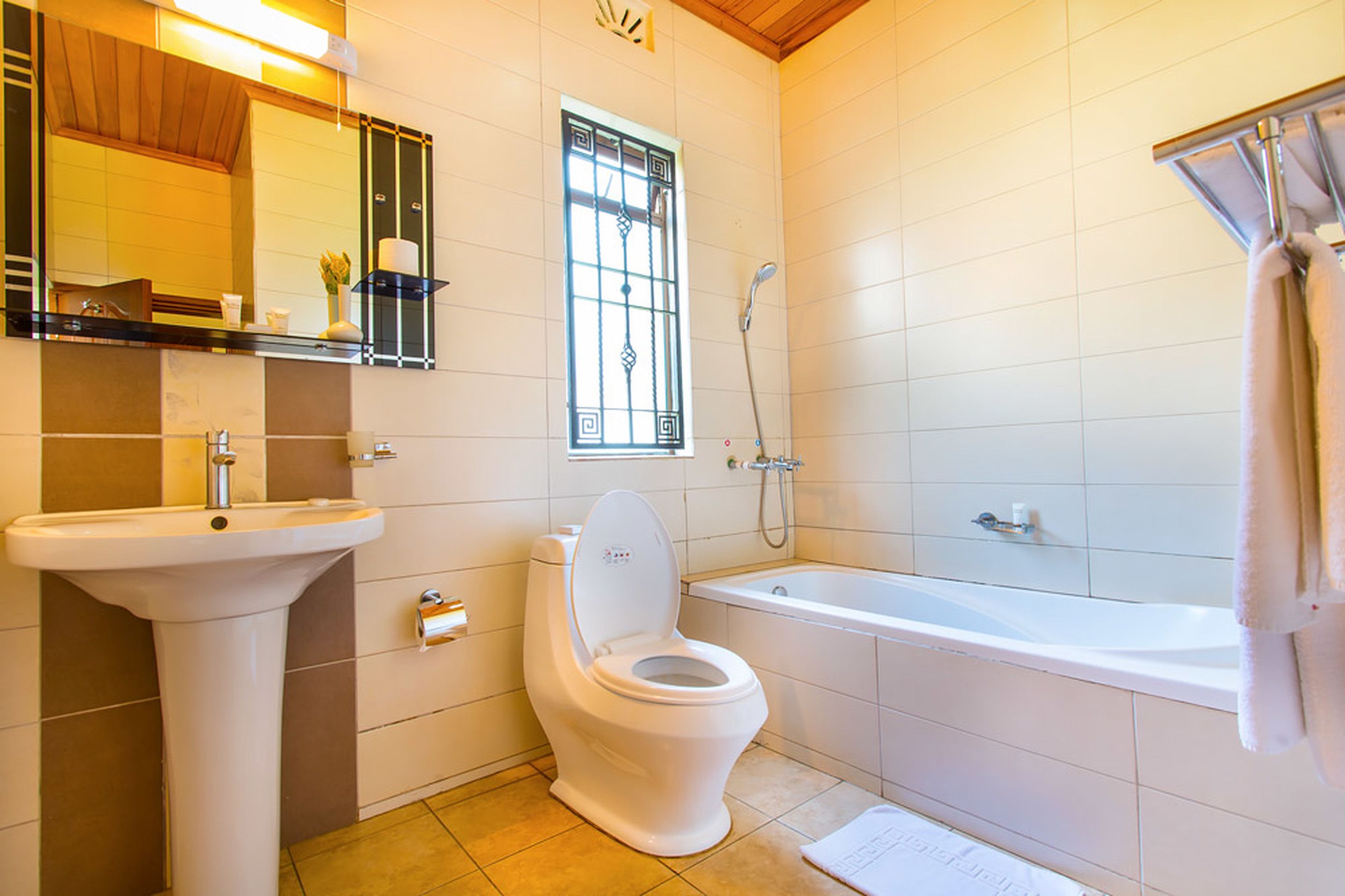 Une salle de bain équipée de toilettes, d’un lavabo, d’une baignoire et d’une fenêtre avec des barreaux.