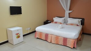 A hotel room with a bed, a small white refrigerator, a bedside table with a phone, and a wall-mounted TV. - Royal City Hotel (Kisumu)