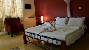 Habitación de hotel con cama, un sillón rojo, mesita de noche con lámpara y televisor montado en la pared.