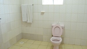 Un baño con azulejos blancos, un inodoro, una toalla colgada en un perchero y una ventana sobre el inodoro.