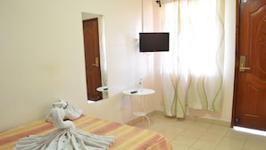 Una habitación de hotel con cama, televisión montada en la pared, una mesita y un espejo.