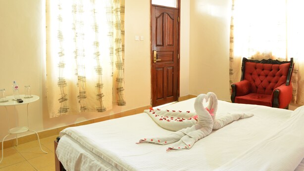 Habitación de hotel con una cama, un sillón rojo, una mesita con una botella y un vaso, y cortinas estampadas con un diseño escocés.