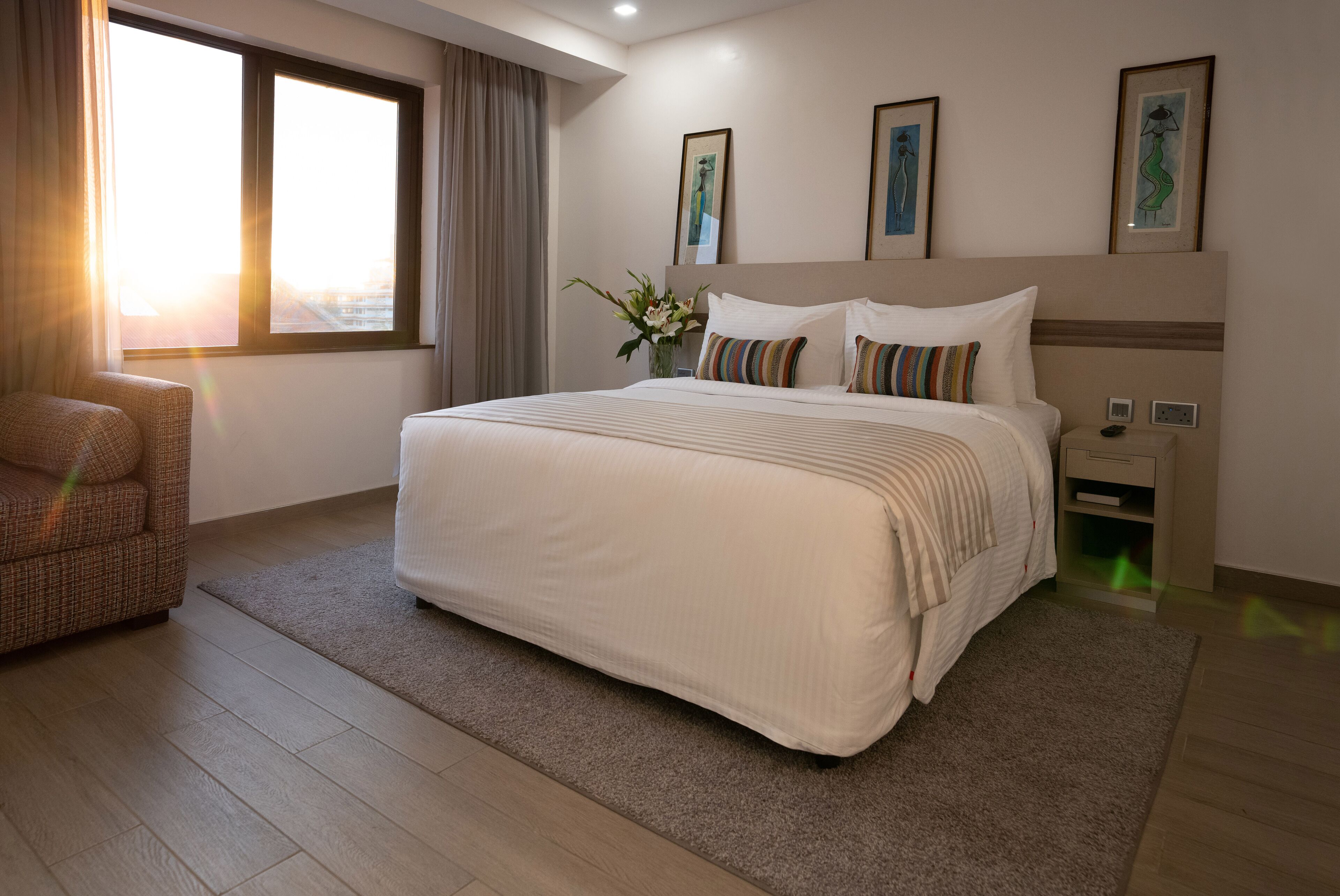 A hotel room with a large bed, a chair, a nightstand, and a window with curtains.