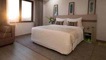 A hotel room with a large bed, a chair, a nightstand, and a window with curtains.