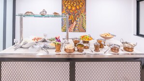 Una mesa de buffet con diversos platos y utensilios, una repisa de cristal con objetos decorativos, y un cuadro colorido en la pared.