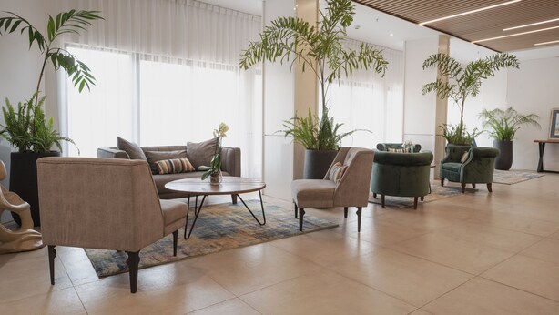 Un hall amplio con diseño moderno, que incluye un sofá, sillones, una mesa de centro y varias plantas en macetas.