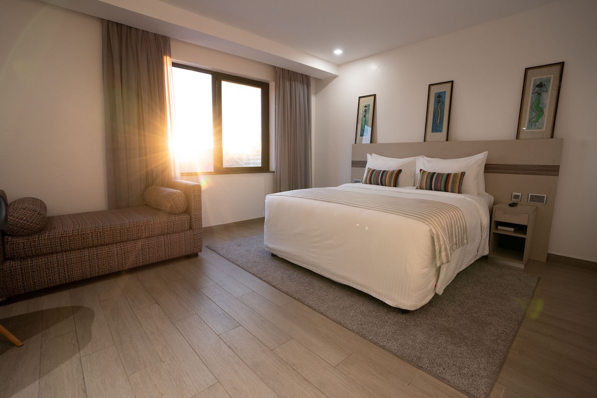 Habitación de hotel moderna con una cama grande, un sofá, una mesita de noche y una ventana con cortinas.
