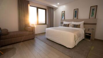 Habitación de hotel moderna con una cama grande, un sofá, una mesita de noche y una ventana con cortinas.