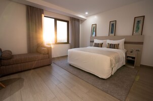Habitación de hotel moderna con una cama grande, un sofá, una mesita de noche y una ventana con cortinas.