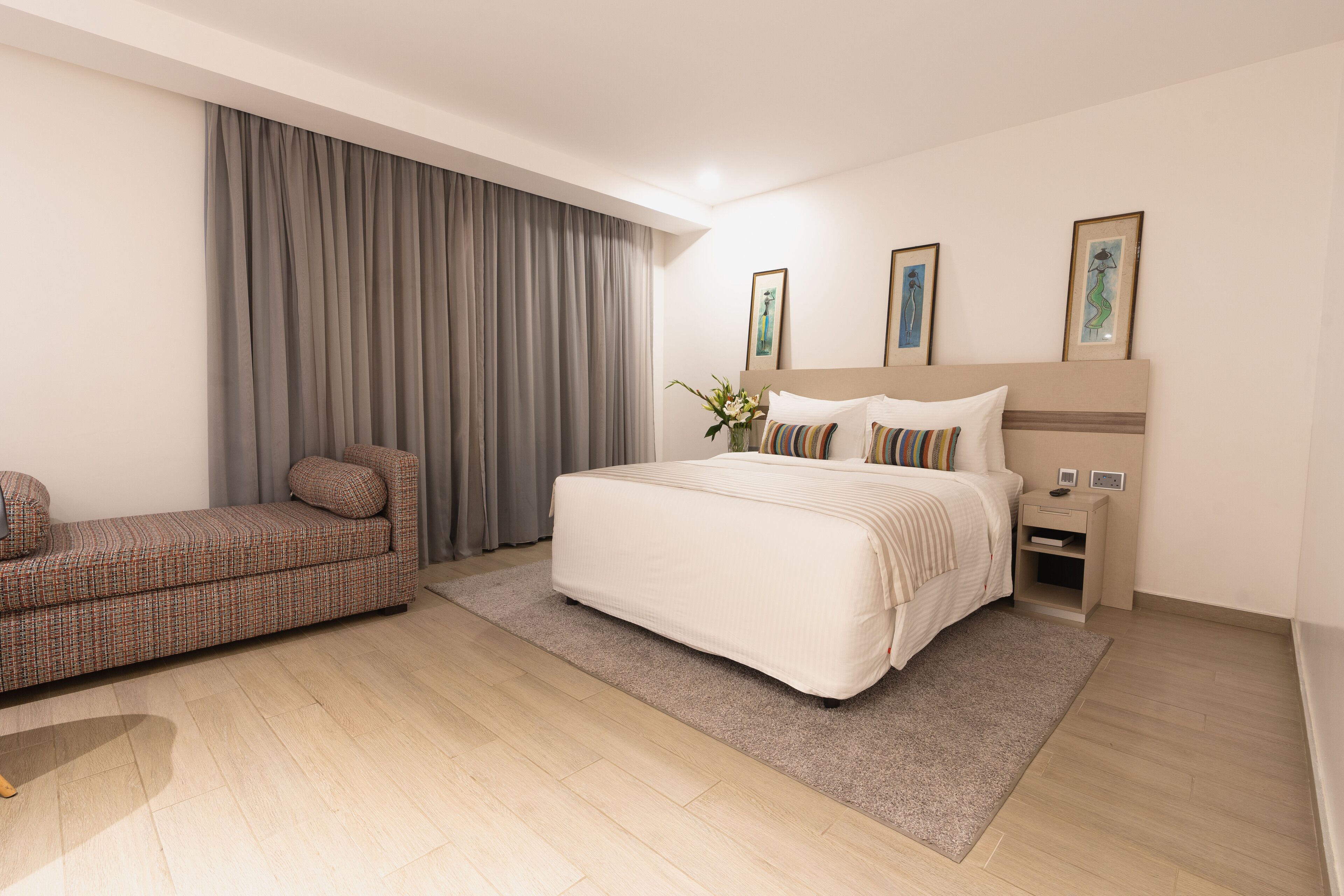A modern hotel room with a large bed, a sofa, and a nightstand.