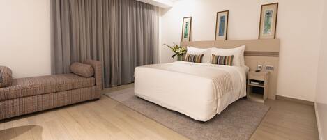 A modern hotel room with a large bed, a sofa, and a nightstand.