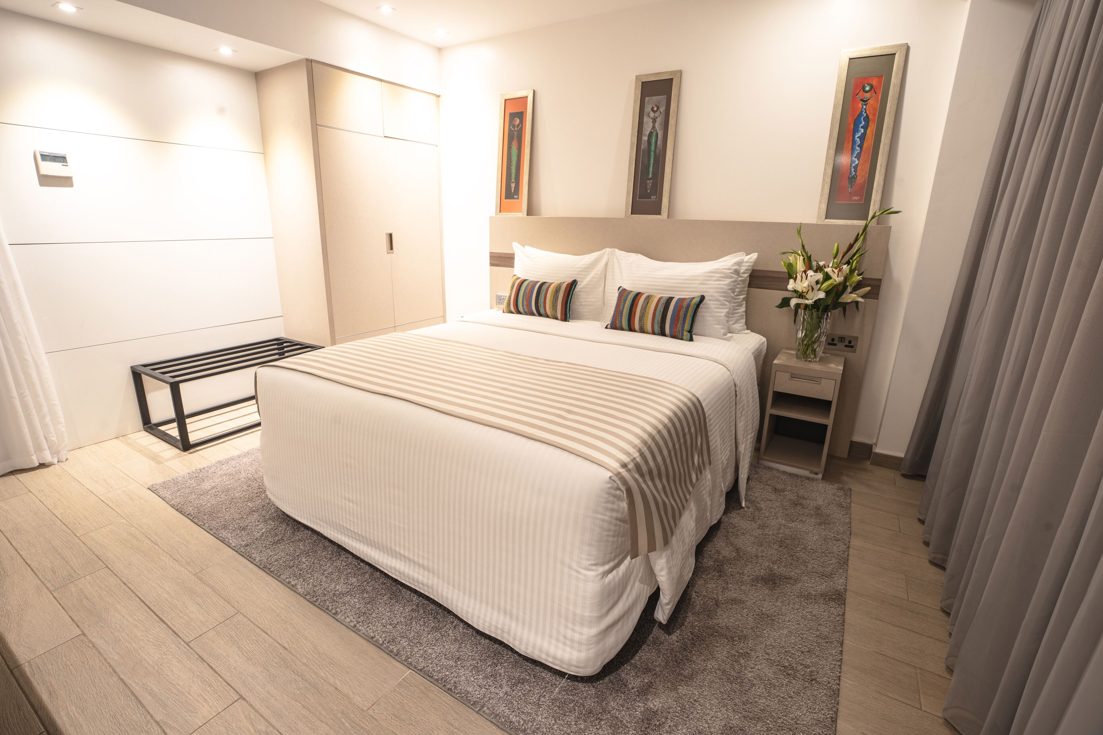 A modern bedroom with a large bed, a bedside table, a nightstand, and a wall-mounted heater.