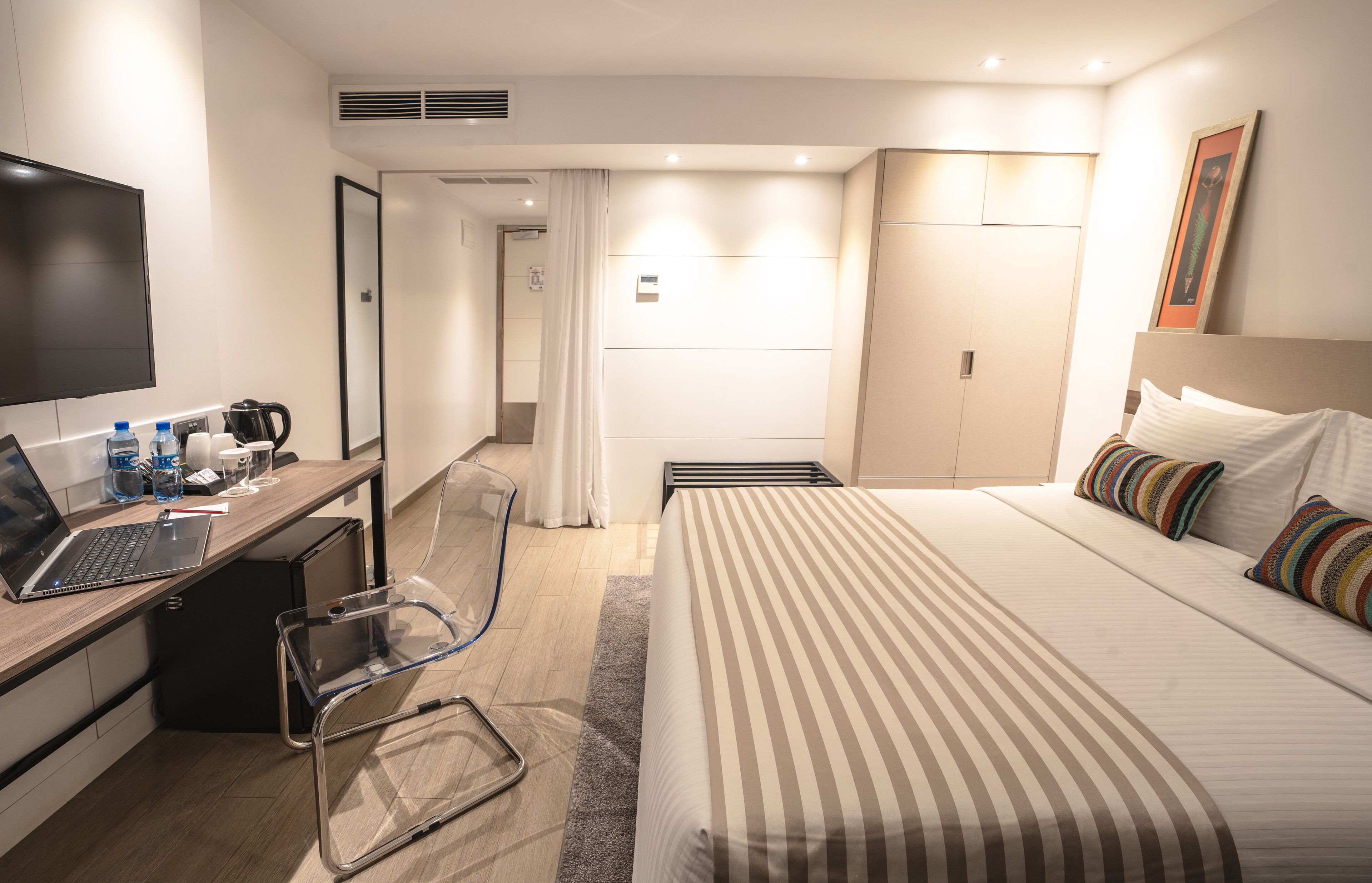 Una camera d'albergo con un letto, una scrivania con un portatile, una sedia, una televisione e un bagno.