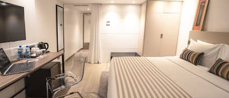 Ein Hotelzimmer mit Bett, Schreibtisch, Laptop, Stuhl, Fernseher und Badezimmer.