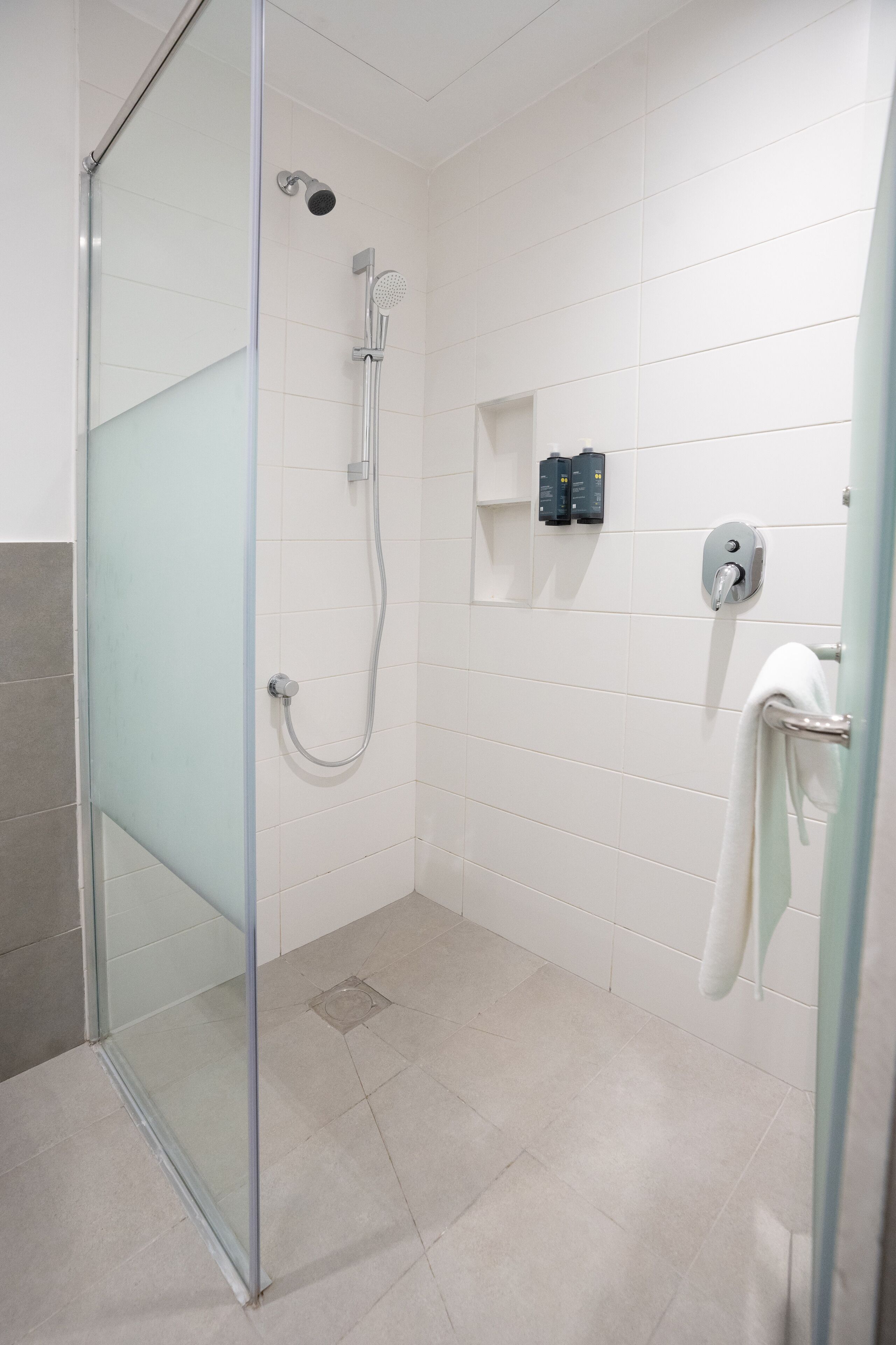 A modern bathroom with a glass shower enclosure, white tiled walls, and a towel rack.