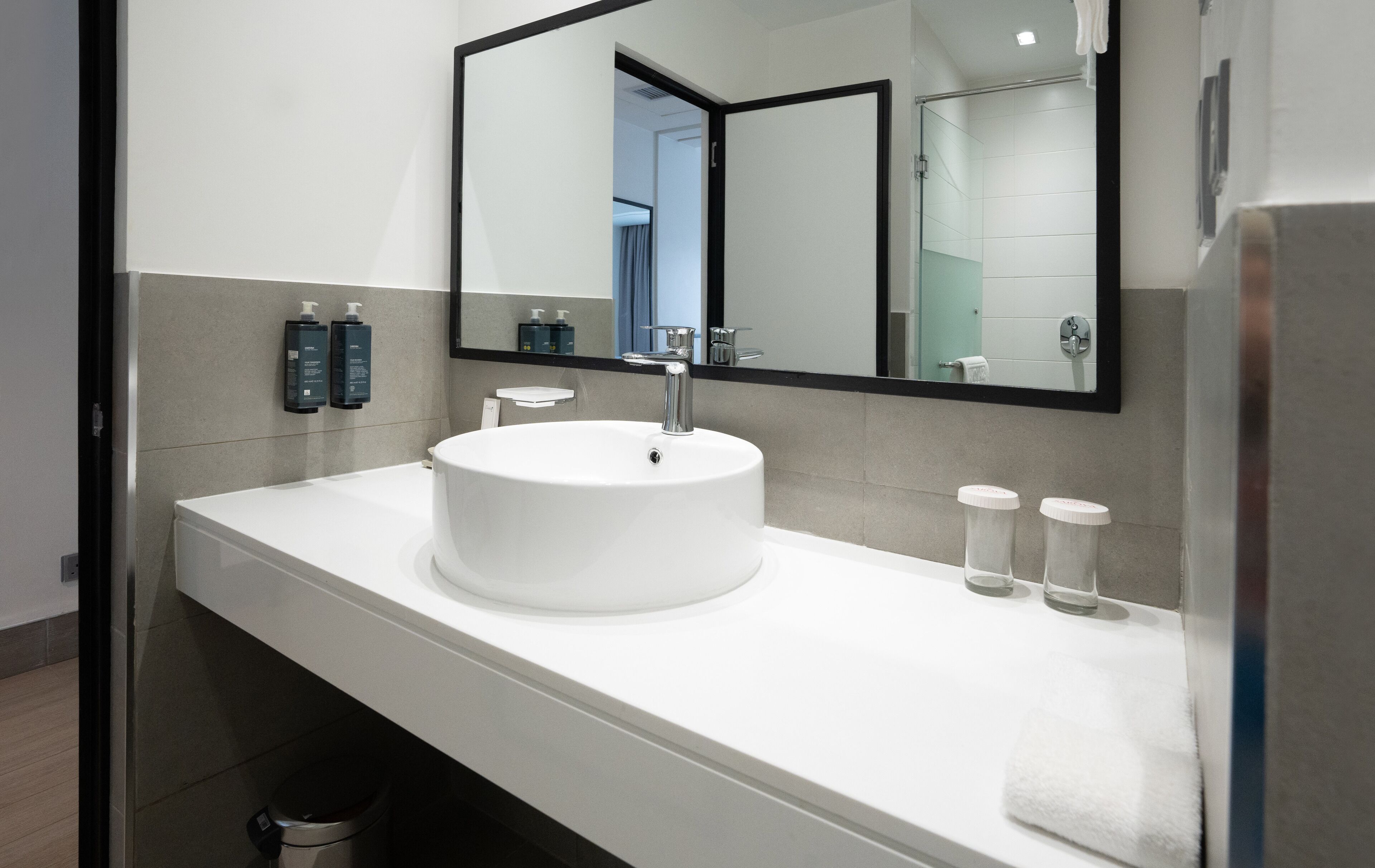 A modern bathroom with a white sink, a large mirror, and two bottles of hand soap.