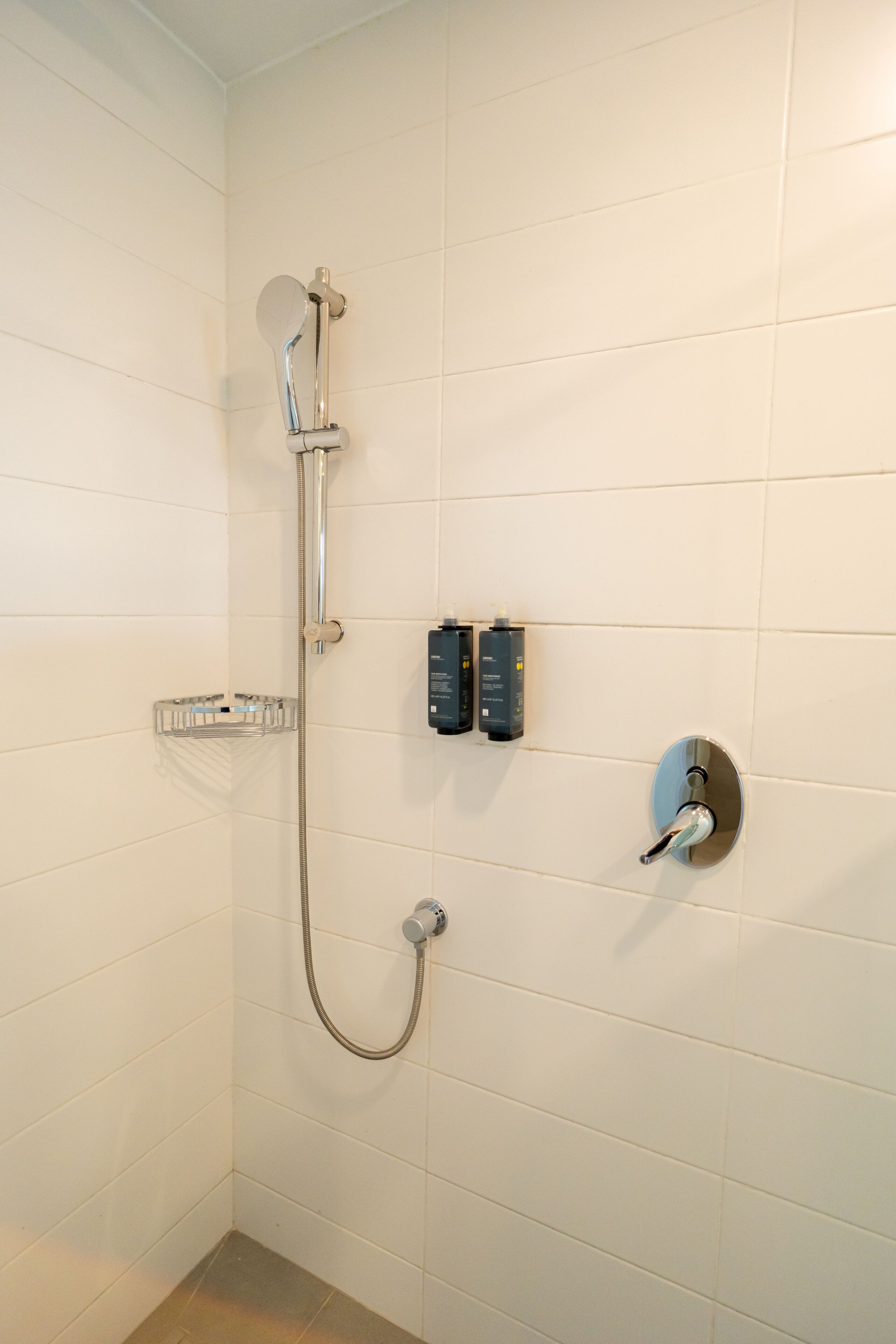 A shower with a handheld showerhead, a wall-mounted control panel, and a soap dispenser.