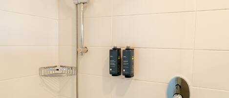 A shower with a handheld showerhead, a wall-mounted control panel, and a soap dispenser.