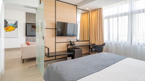 Una habitación de hotel moderna con una cama grande, un escritorio con computadora, una silla, un televisor y un separador de vidrio.