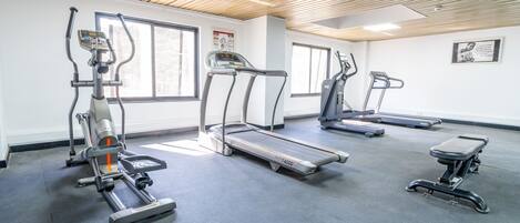 Un gimnasio con cintas de correr, elípticas y una banca.