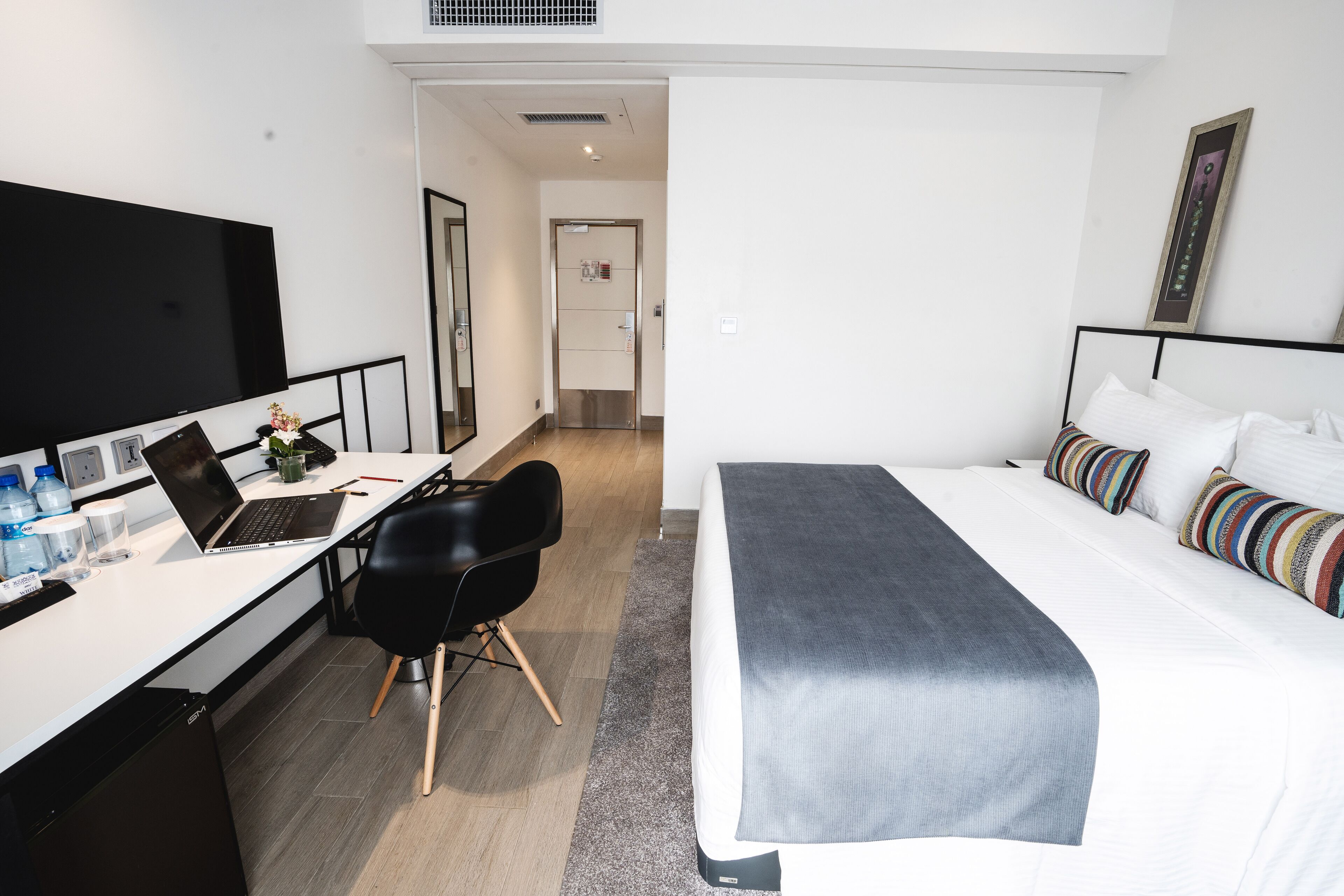 A modern hotel room with a bed, a desk with a laptop, a chair, and a TV.