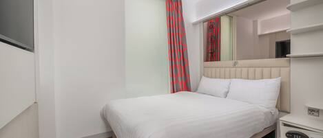 A hotel room with a bed, a bedside table with a control panel, a mirror above the bed, and a sliding door with a red and gray curtain.