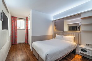 A hotel room with a bed, a TV, a microwave, and a built-in wardrobe.
