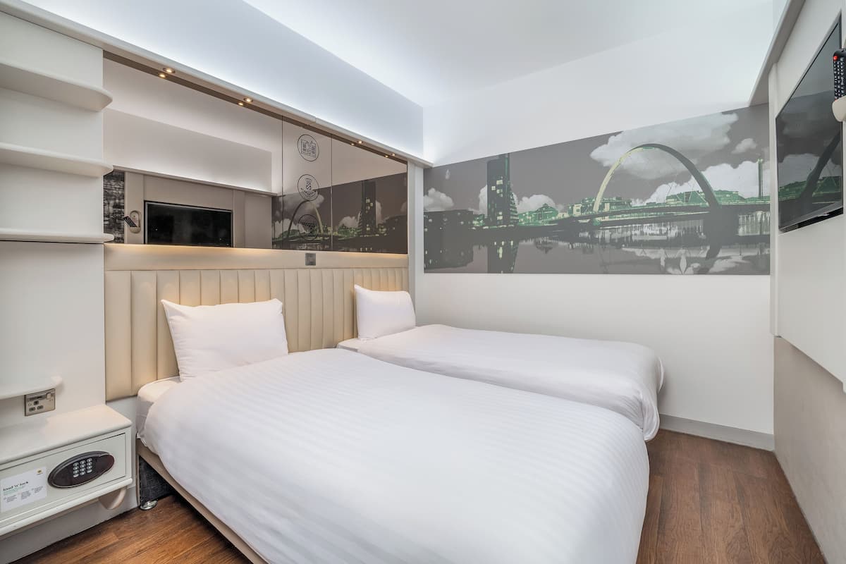 A hotel room with a bed, bedside table, TV, and a cityscape mural.