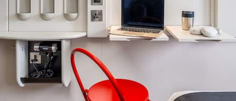 A modern hotel room with a white desk, a laptop, a red chair, and a coffee machine.