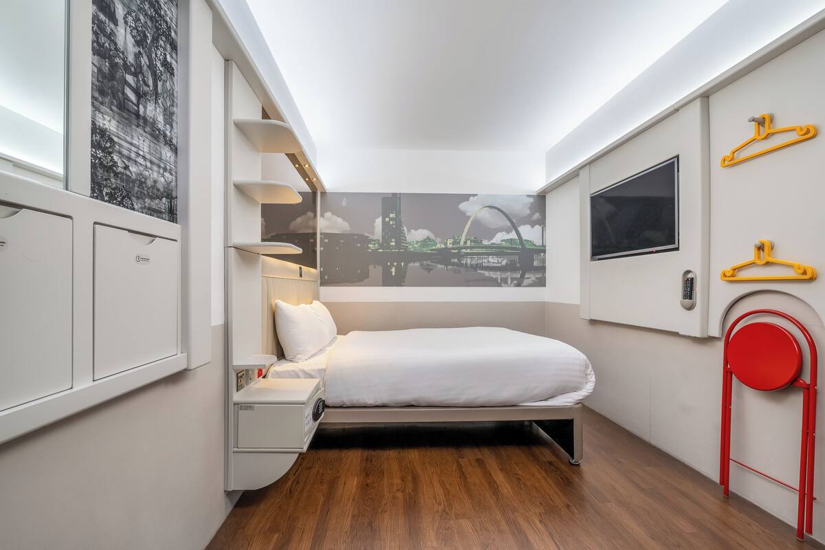 A compact hotel room with a bed, bedside table, and a wall-mounted TV.