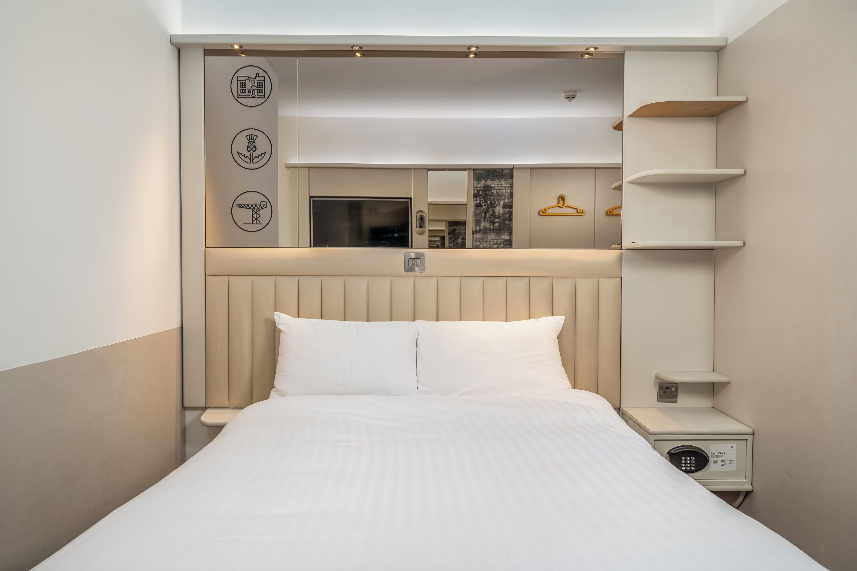 Una camera d'albergo con un letto, un comodino e una mensola a parete.