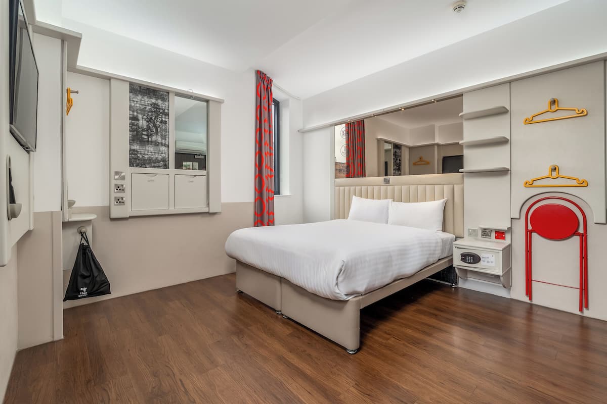 A modern hotel room with a bed, a bedside table, a mirror, and a wardrobe.