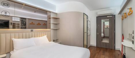 A modern hotel room with a large bed, built-in shelving, a wardrobe, a mirror, and a bathroom door.