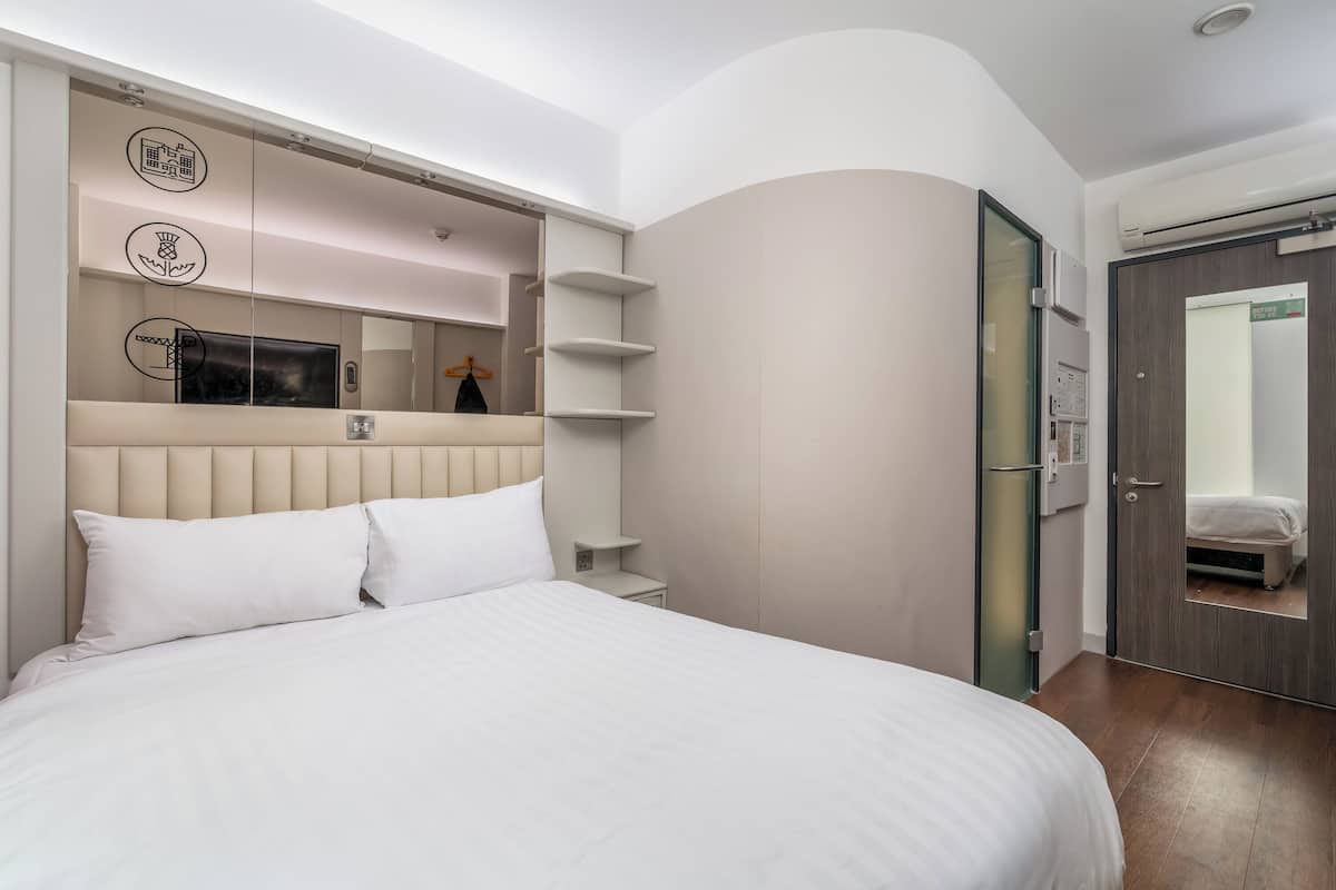 A modern hotel room with a large bed, built-in shelves, a mirror, and a wardrobe.