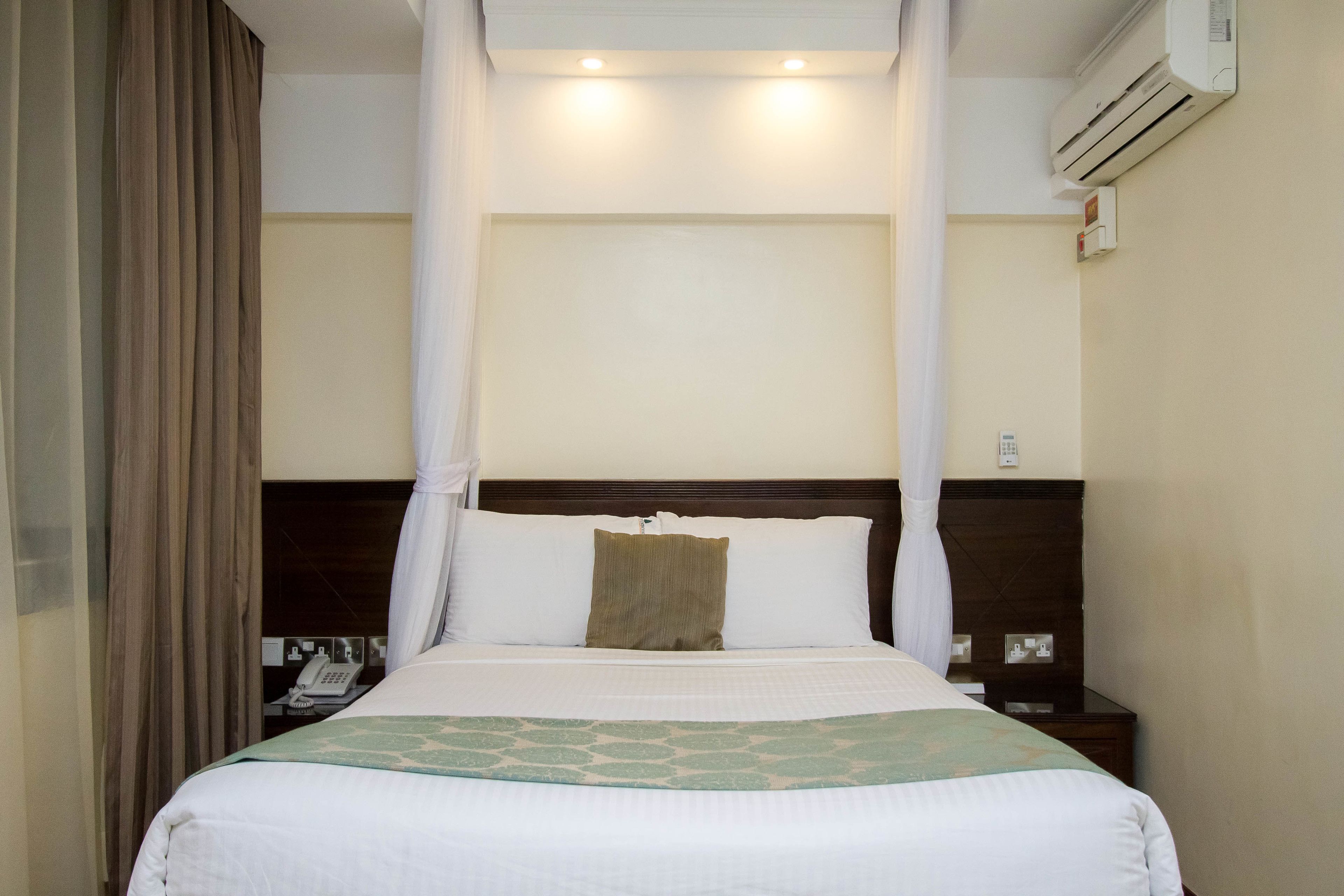 A hotel room with a bed, a nightstand, an air conditioning unit, and a curtain.