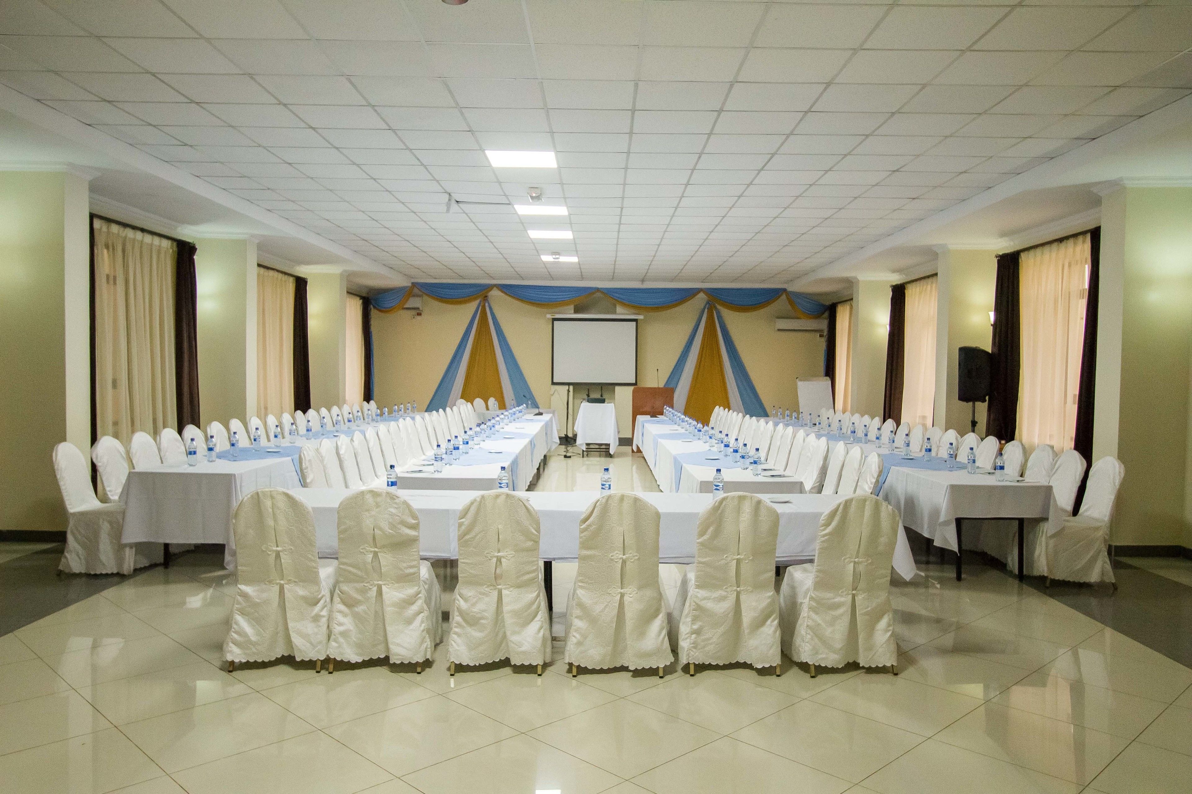 A conference room with long tables, white chairs, and a projector screen.