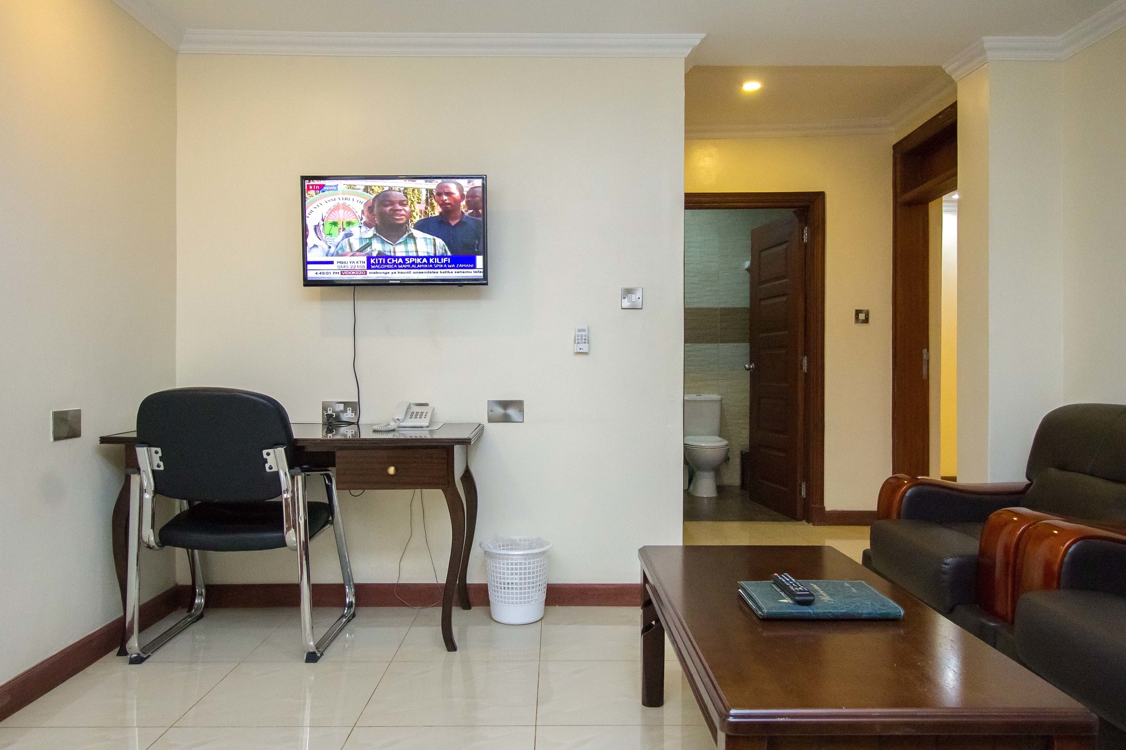 A living room with a television mounted on the wall, a desk with a chair, a sofa, and a coffee table.