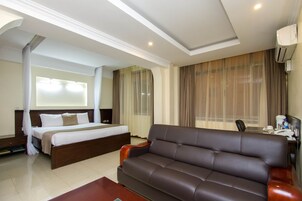 Una habitación de hotel con cama, sofá, escritorio con silla y ventana con cortinas.