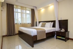 A hotel room with a large bed, a nightstand, a TV, and a window with curtains. - Pinecone Hotel (Kisumu)